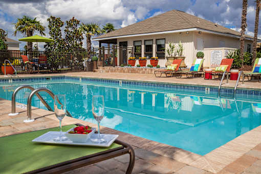 A poolside table with a plate of food and two glasses of wine.