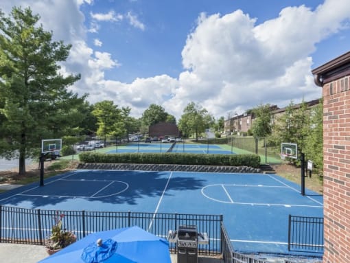 a blue tennis court with two basketball courts in the background and a barbecue grill in the foreground