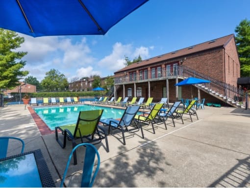 a swimming pool with chaise lounge chairs and umbrellas in front of a brick building