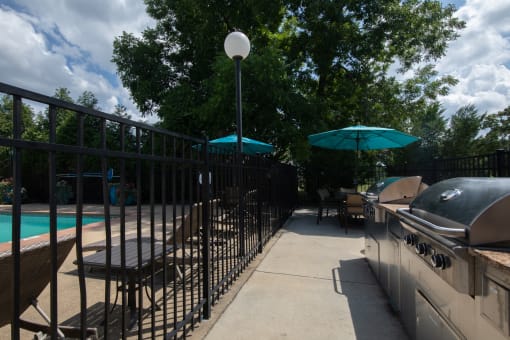a backyard with a grill and table and chairs and a pool in the background