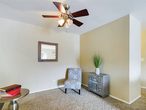 A room with a ceiling fan, a chair, a small table, and a plant.