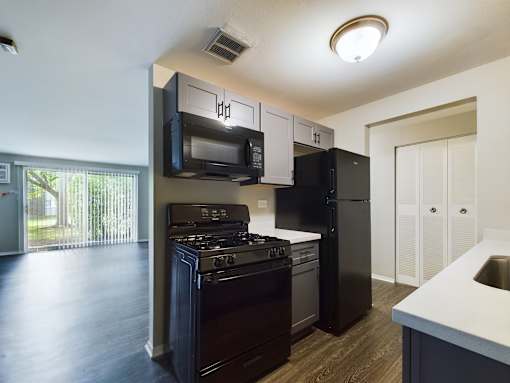 A modern kitchen with dark wood floors and black appliances.