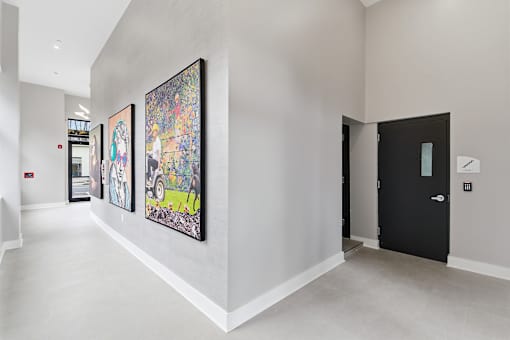 Three paintings hang on a wall in a white hallway.