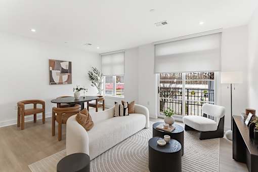 A modern living room with a white sofa, wooden chairs, and a coffee table.