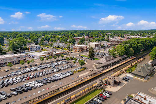 A train station with a train on the tracks and cars parked in the lot.