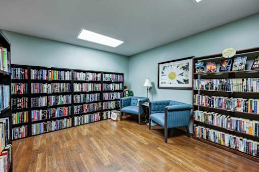 A room full of books with a blue chair and a lamp.