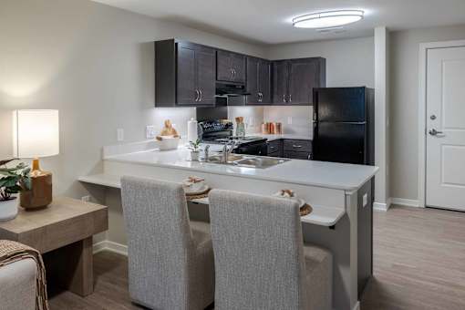 A kitchen with a black refrigerator and grey chairs.