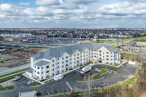 A large white building with a grey roof is surrounded by a parking lot.
