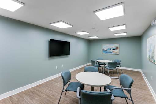 A room with a table and chairs and a television on the wall.