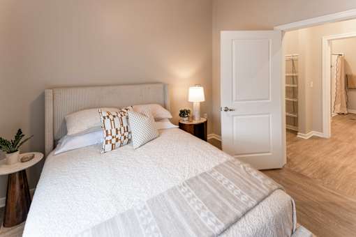 A bedroom with a large bed and a small table with a lamp on it.