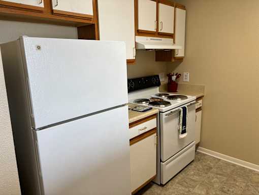 A white refrigerator stands in a kitchen with a stove and oven.