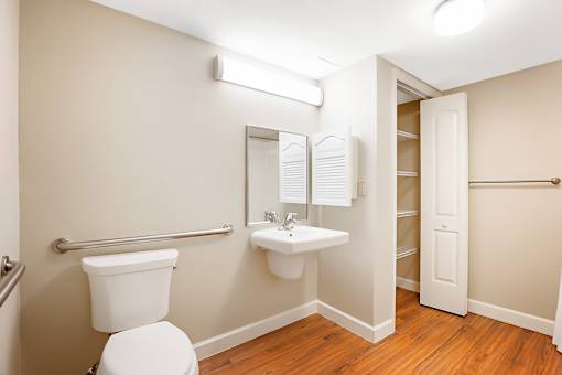 A bathroom with a toilet, sink, mirror, and a towel bar.