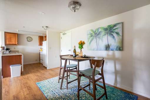 A dining room with a table and chairs and a painting of a palm tree on the wall.