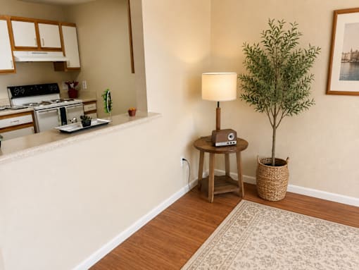 A small tree in a basket sits on a table next to a lamp in a kitchen.