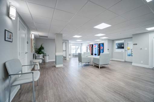 A spacious waiting room with white chairs and a plant.