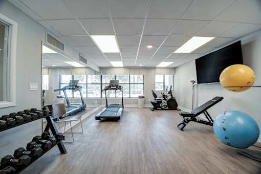 A gym with a variety of equipment including a treadmill, dumbbells, and a bench press.