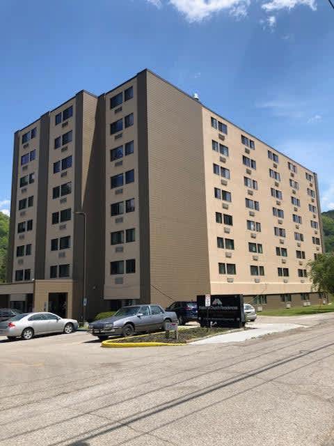 A large tan building with many windows sits next to a parking lot.