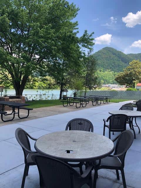 A patio with tables and chairs overlooking a lake.