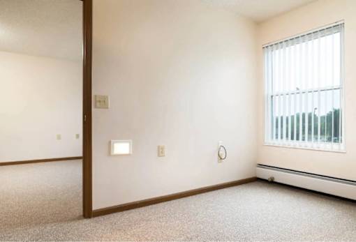 A room with a window, carpeted floor, and a door.