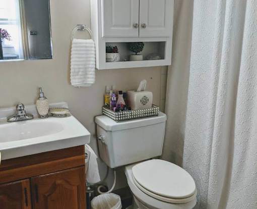 A white toilet is in a small bathroom with a white sink and a white cabinet.