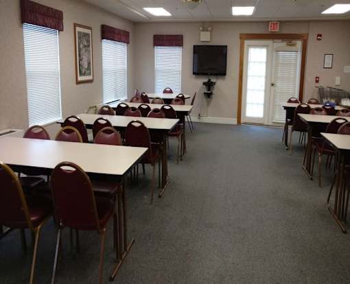 A room with tables and chairs and a TV on the wall.