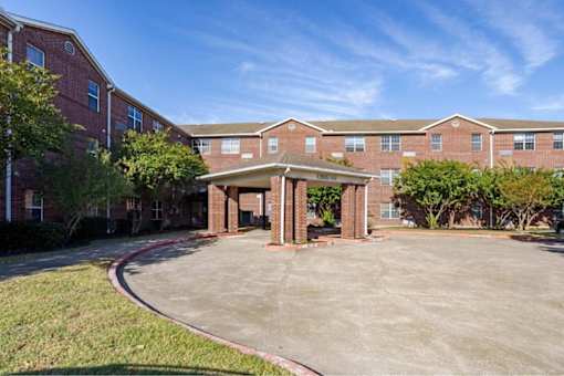 A parking lot in front of a brick building with a covered walkway.