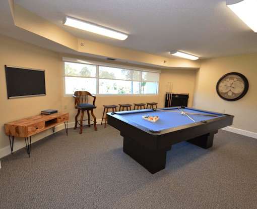 A pool table is in the middle of a room with a TV and a clock on the wall.