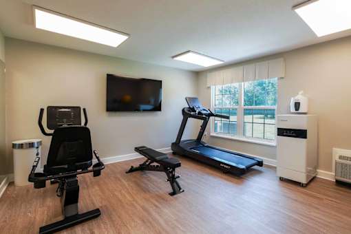 A home gym with a treadmill, rowing machine, and a television.