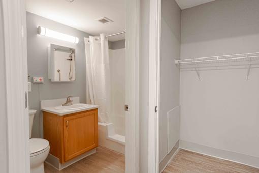 A bathroom with brand new toilet, sink, and a mirror. To the right is the large hall closet.
