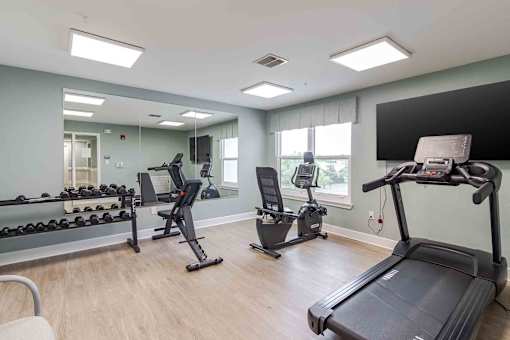 A spacious gym with treadmills, elliptical machines, and dumbbells.