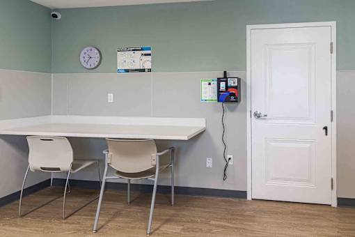 A white table with two chairs in a room with a clock on the wall.