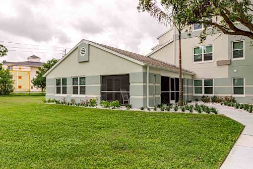 A white building with a brown roof is surrounded by a green lawn.