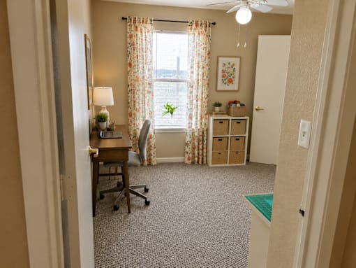 A room with a desk, chair, and a window with curtains.