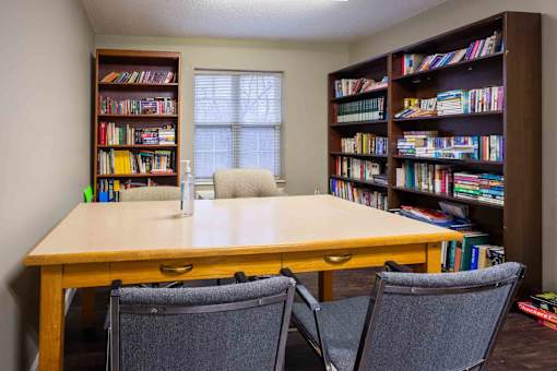 A room with a table, chairs, and bookshelves filled with books.