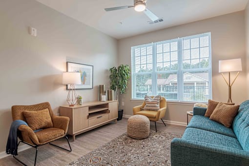 A living room with a blue couch, a chair, a table, and a ceiling fan at Sweetwater Point in Douglasville, GA.