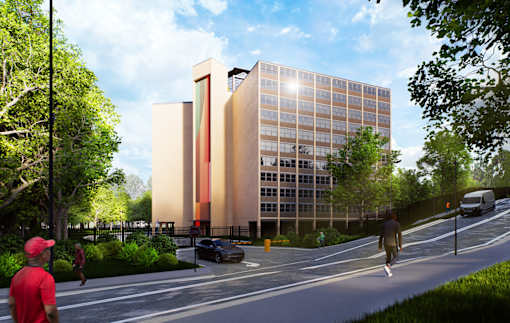 A modern building with a red and orange facade is surrounded by trees and a street with people walking.