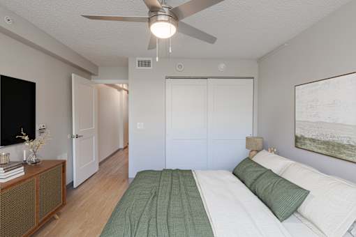 A bedroom with a bed, a ceiling fan, and a painting on the wall.