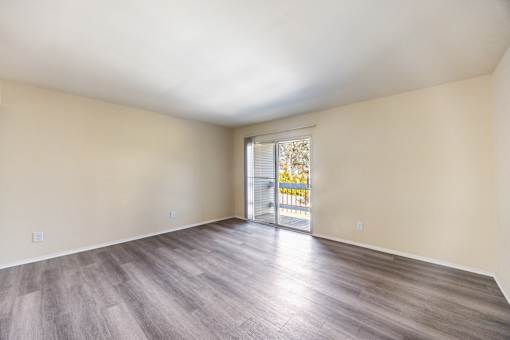 A room with wooden flooring and a sliding glass door leading to a balcony.