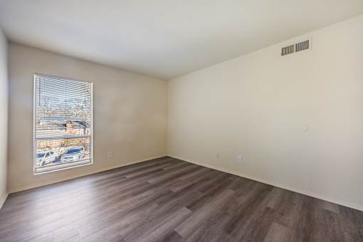 A room with wooden flooring and a window showing a parking lot outside.