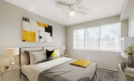 A bedroom with a bed, a ceiling fan, and a painting on the wall.