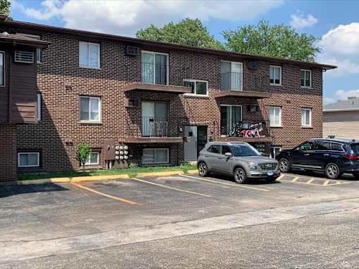 A parking lot in front of a brown brick apartment building with two cars parked.