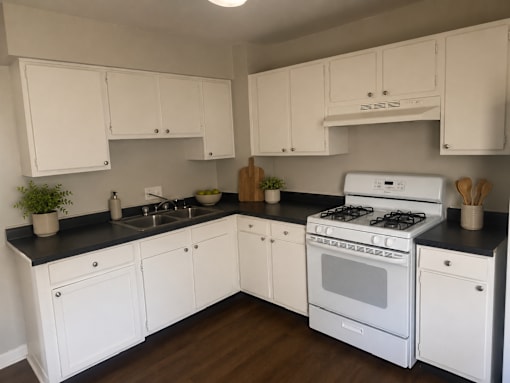 A white kitchen with black countertops and wooden floors.