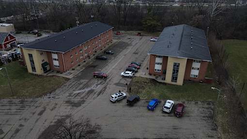 A parking lot with cars and two buildings in the background.