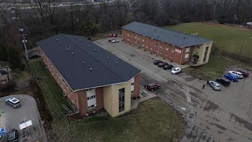 A large building with a black roof is surrounded by a parking lot.