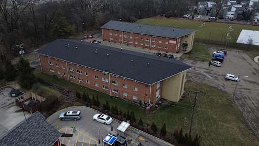 A large red brick building with a black roof and a parking lot in front.