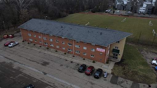 A red brick building with a black roof and a parking lot in front.