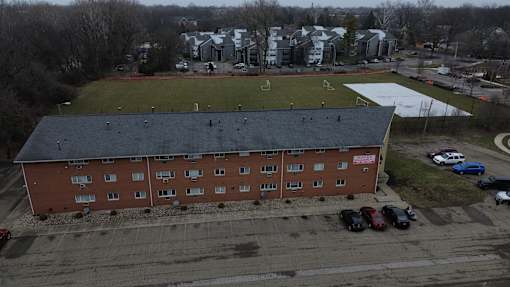 A red brick building with a black roof is surrounded by a parking lot.
