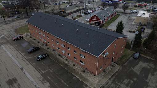 A red brick building with a black roof is surrounded by a parking lot.