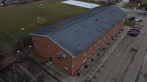 A red brick building with a grey roof is surrounded by a parking lot.
