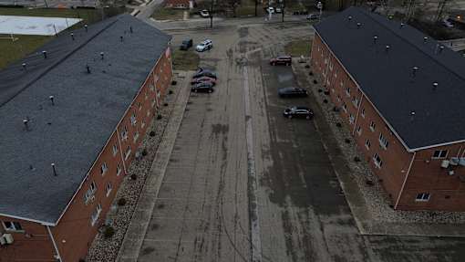 A parking lot is in the middle of two red brick buildings.